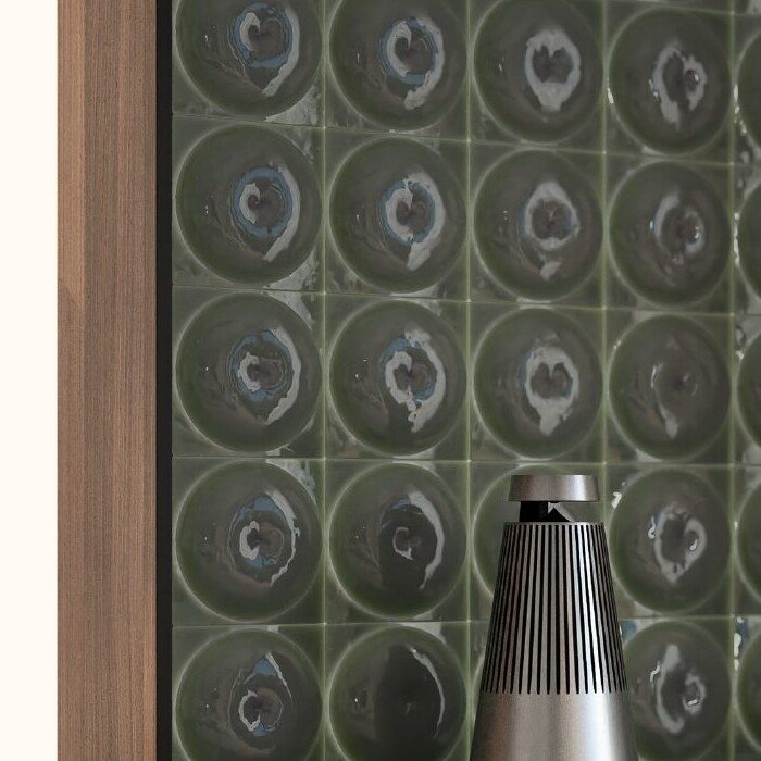 Close-up of a Bang & Olufsen Beolab speaker in front of a dark green glazed ceramic tile wall